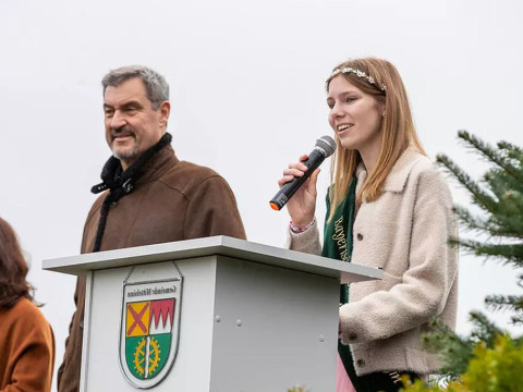 Markus Söder eröffnet die Christbaumsaison bei Christbaum-Klug Markus Söder steht an einem Rednerpult neben der bayerischen Christbaumkönigin Sina Klug