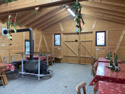Gemütlicher Innenraum der Holzhütte mit Holzofen und festlich geschmücktem Tisch im Christbaumdorf