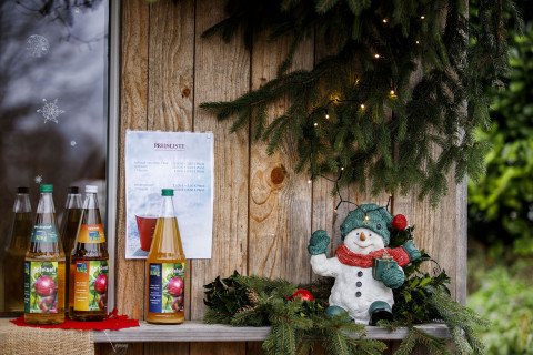 Weihnachtliche Atmosphäre für individuelle Firmenpräsente bei Christbaum Klug Weihnachtlich dekorierter Bereich an einer Holzhütte mit Getränkeflaschen und Tannenzweigen
