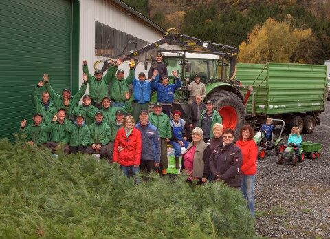 Das Team von Christbaum-Klug am Hauptstandort Mittelsinn Gruppenfoto von Männern und Frauen in grüner Arbeitskleidung vor einer Halle mit Traktor und aufgestapeltem Tannengrün