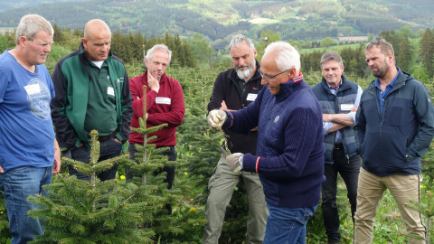 Hans Koch zeigt einer Gruppe von Männern und Frauen zwischen Weihnachtsbäumen eine Bodenprobe